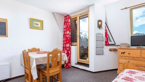Ein Zimmer mit Holztisch und -stühlen, einem Bett, einem Schminktisch, einem Fernseher und einem Fenster mit Blick auf die Berge.