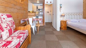A cozy room with a wooden sofa, a small dining table, a bed with a white headboard, and a kitchen area in the background. - Cozy apartment for 4 in Avoriaz with southeast-facing balcony (Avoriaz)