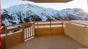 Varanda com guarda de madeira com vista para uma cordilheira coberta de neve.