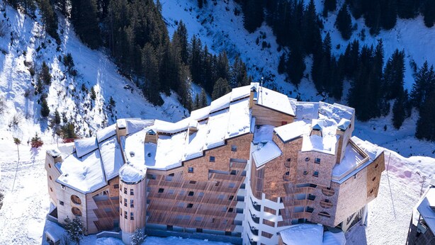 Um edifício grande e de vários andares com um design arquitetônico singular, cercado por paisagem nevada e árvores.