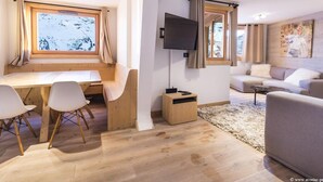 Uma sala de estar moderna com uma escrivaninha de madeira, um sofá, uma televisão e janelas amplas com cortinas.