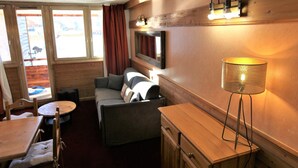 Un interior de cabaña acogedor con un sofá, una mesita, una lámpara y un armario de madera.