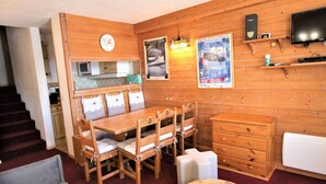 Un cuarto acogedor con una mesa de comedor de madera, sillas, un sofá, una pequeña mesa redonda, un televisor y una zona de cocina con un microondas.