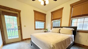 Un dormitorio con una cama, dos ventanas con persianas, una puerta y un ventilador de techo.