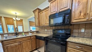 Una cocina con armarios de madera, una estufa negra, un microondas y un lavavajillas.