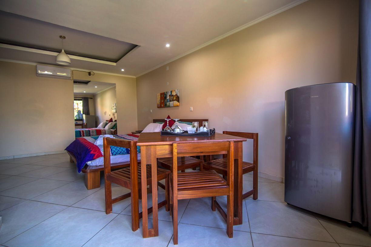 A spacious living area with a wooden dining table, chairs, a sofa, and a refrigerator.