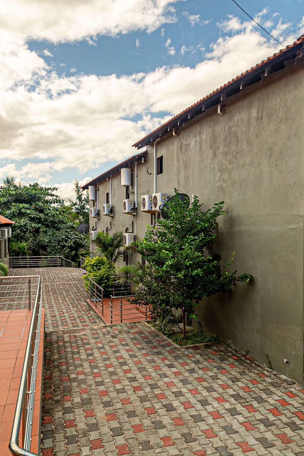 Un patio con un sendero pavimentado, un edificio con varias unidades de aire acondicionado y un cielo despejado.