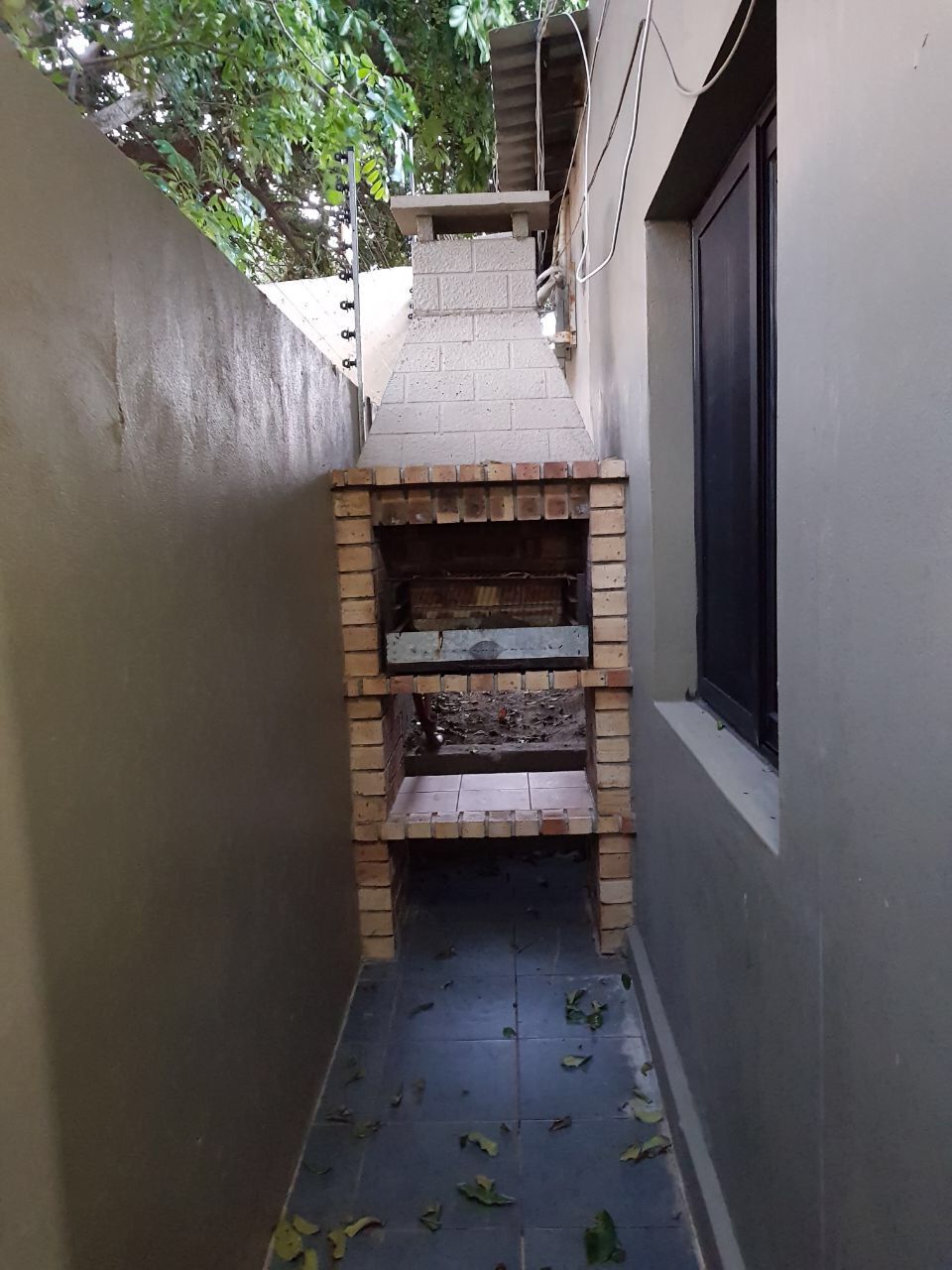 A narrow outdoor space with a brick oven, a window, and a wall.