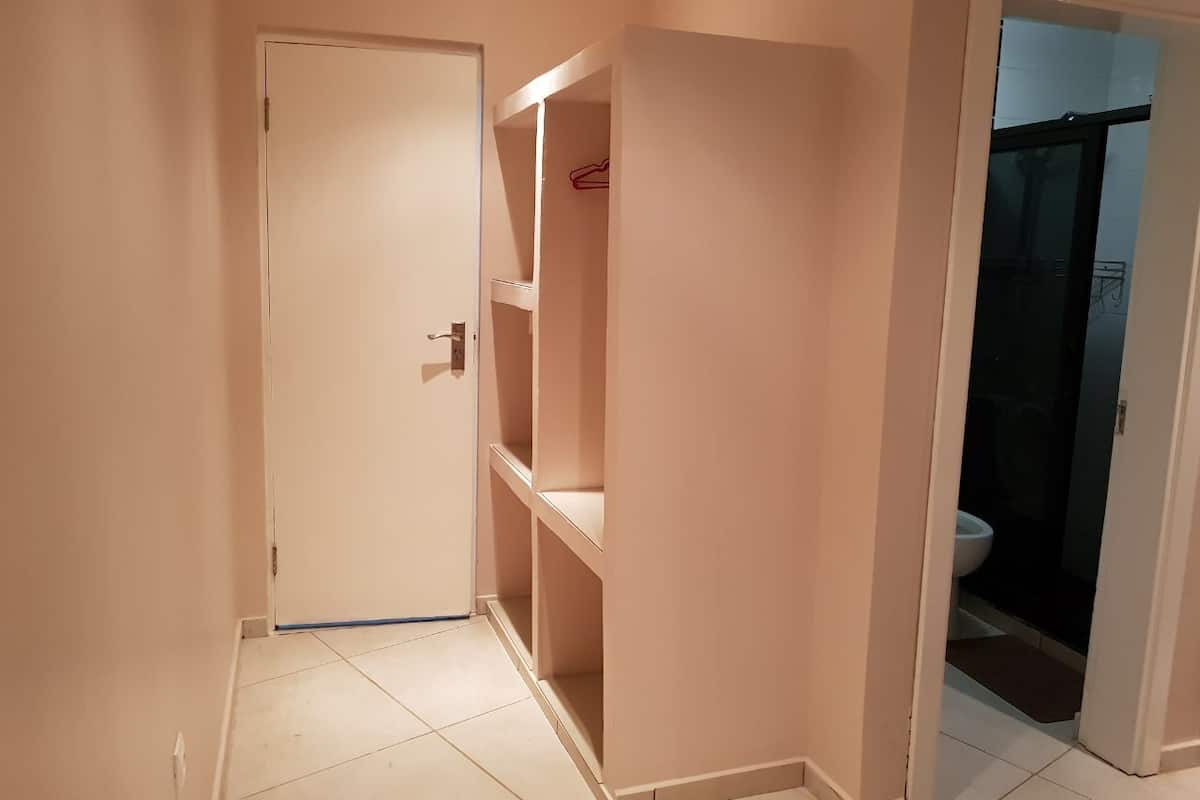 Un pasillo con una puerta cerrada, un armario con estantes y un baño visible a través de una puerta abierta.