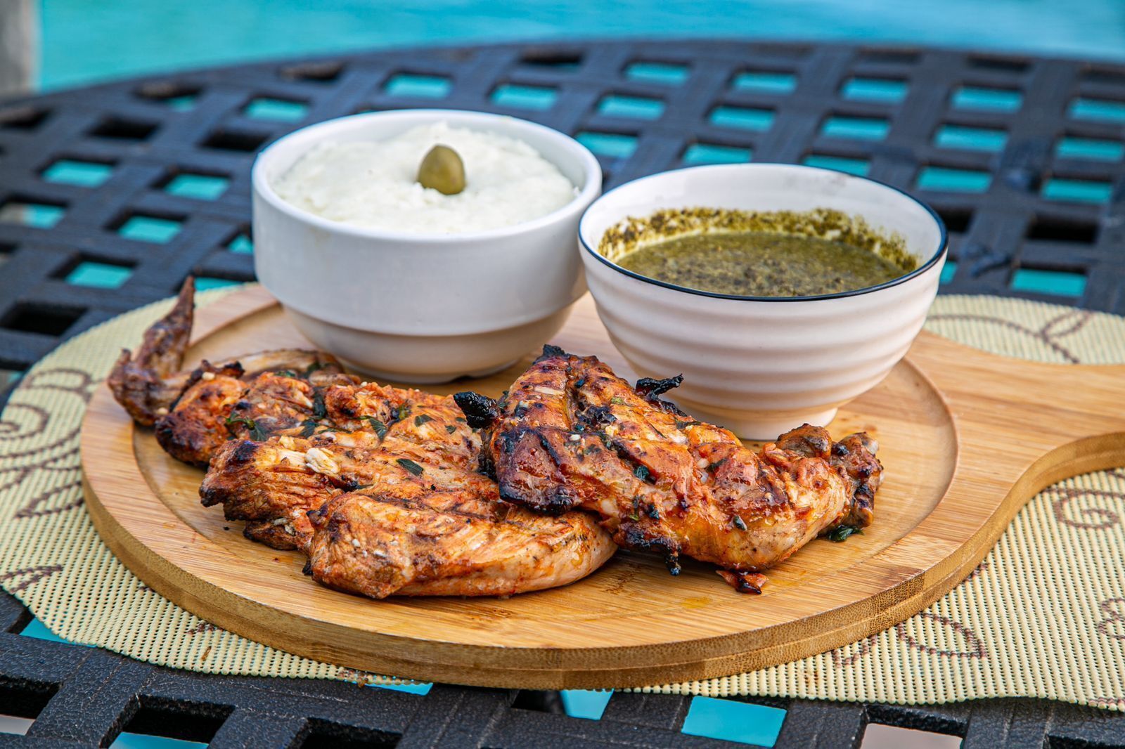 Pollo a la parrilla con dos guarniciones sobre una tabla de madera.