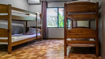 Una habitación con literas, suelo de baldosas, ventana con cortinas y un equipo de aire acondicionado.