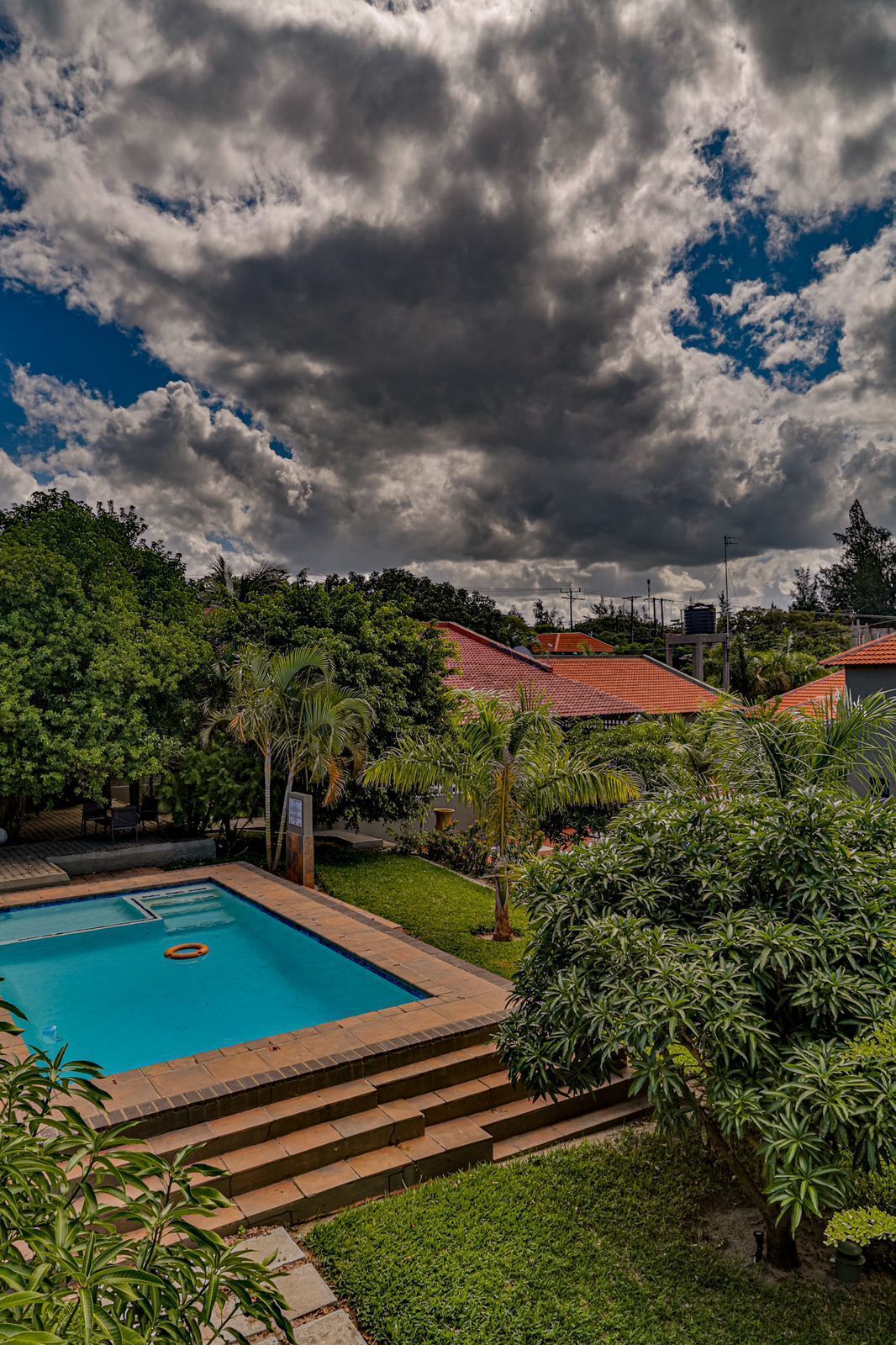 A swimming pool surrounded by lush greenery and a red-roofed building.