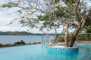 A pool with a tree in the center, surrounded by a tiled deck and a view of the sea. - OSSANZAIA BILENE LODGE (Praia do Bilene)