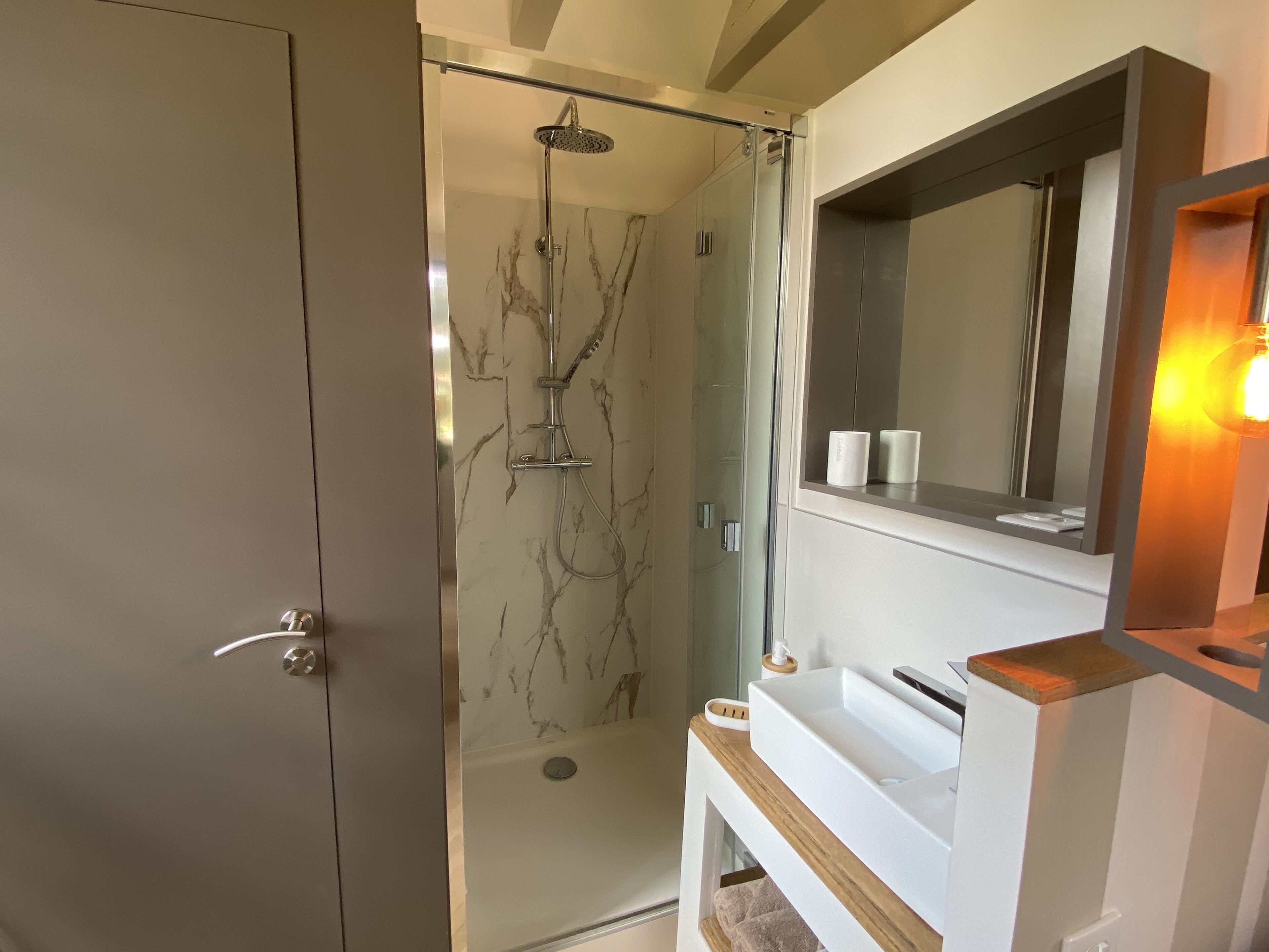 A modern bathroom with a glass-enclosed shower, a white sink, and a mirror above the sink.