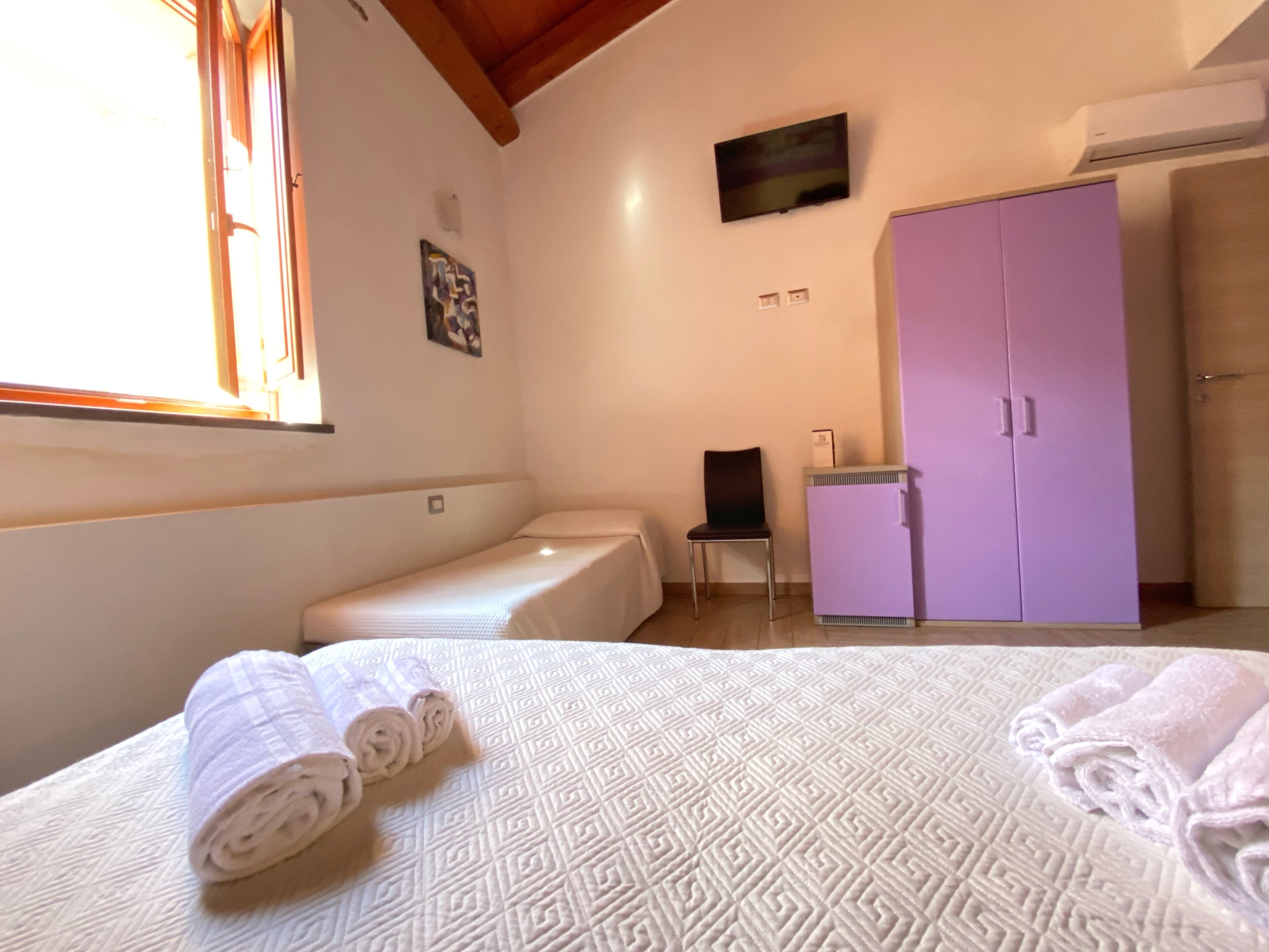Een slaapkamer met een bed, een stoel, een paarse kast en een televisie aan de muur.