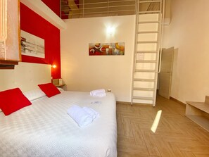 A hotel room with a bed, red pillows, a white headboard, a painting on the wall, a ladder, and a door. - Gioia Guesthouse (Cabras)