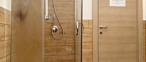 Une salle de bain aux murs lambrissés, dotée d’une douche en verre et d’une porte avec une serrure et une pancarte.