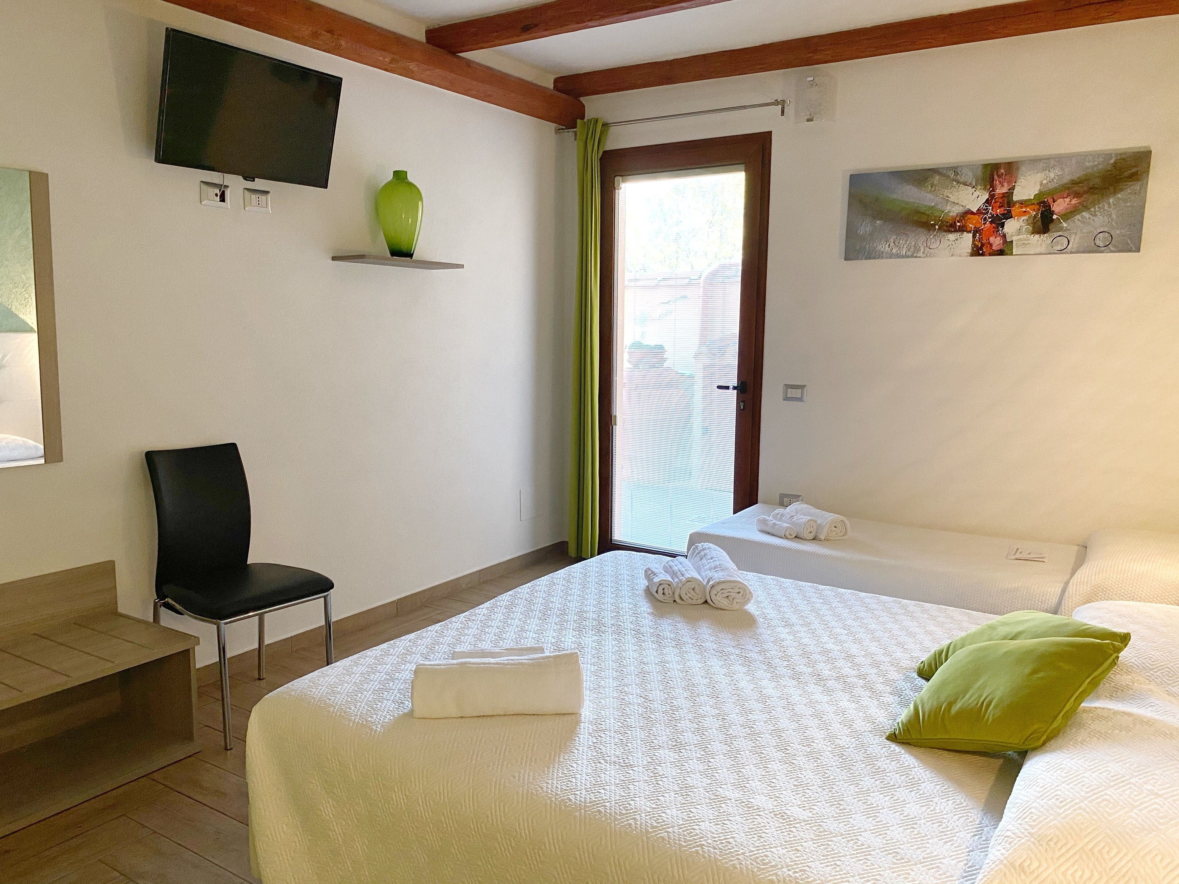 A hotel room with a bed, a chair, a TV mounted on the wall, and a painting.