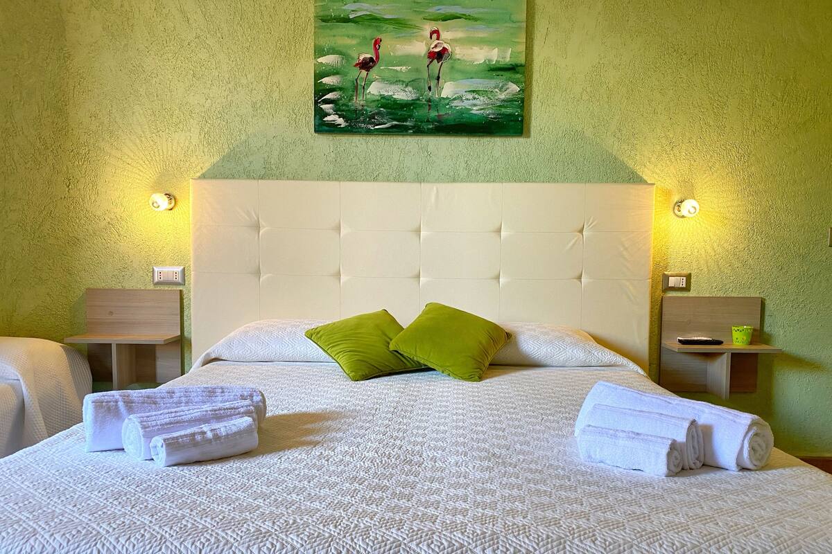 A hotel room with a large bed, two pillows, a painting above the bed, and bedside tables with lamps.