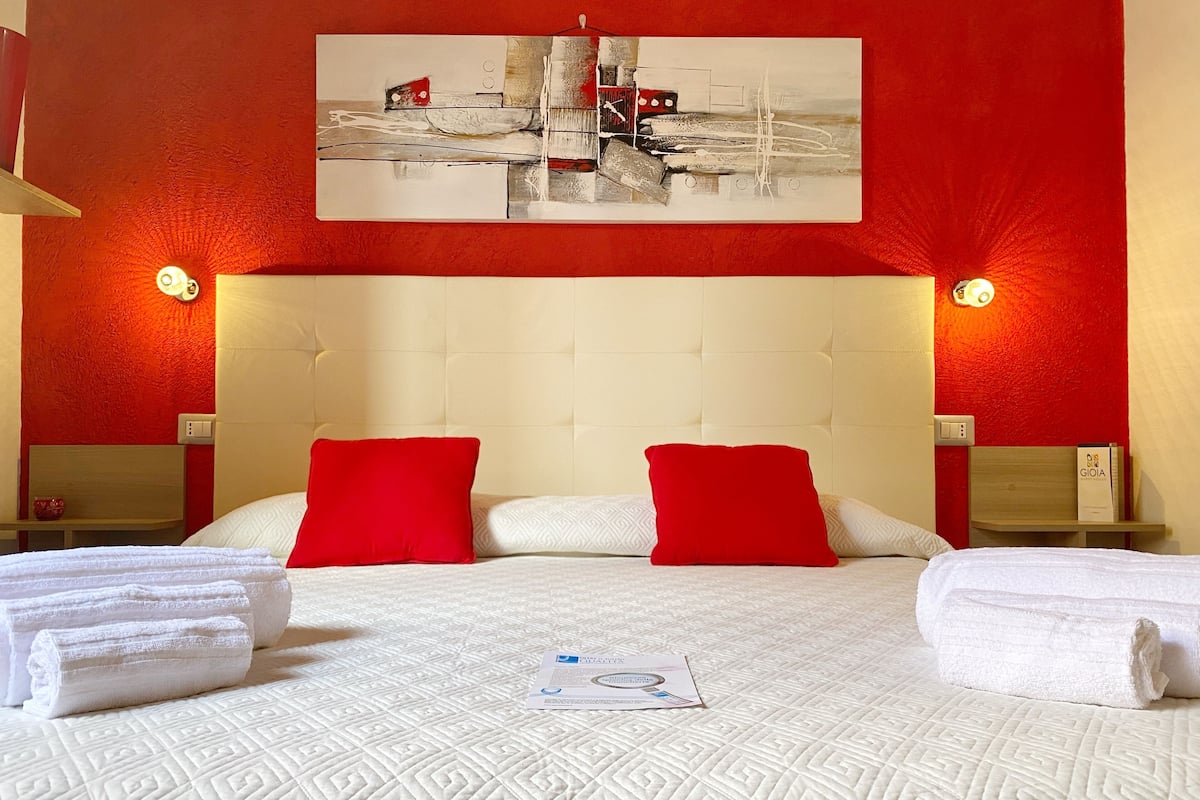 A hotel room with a large bed, red and white pillows, and two nightstands with lamps.