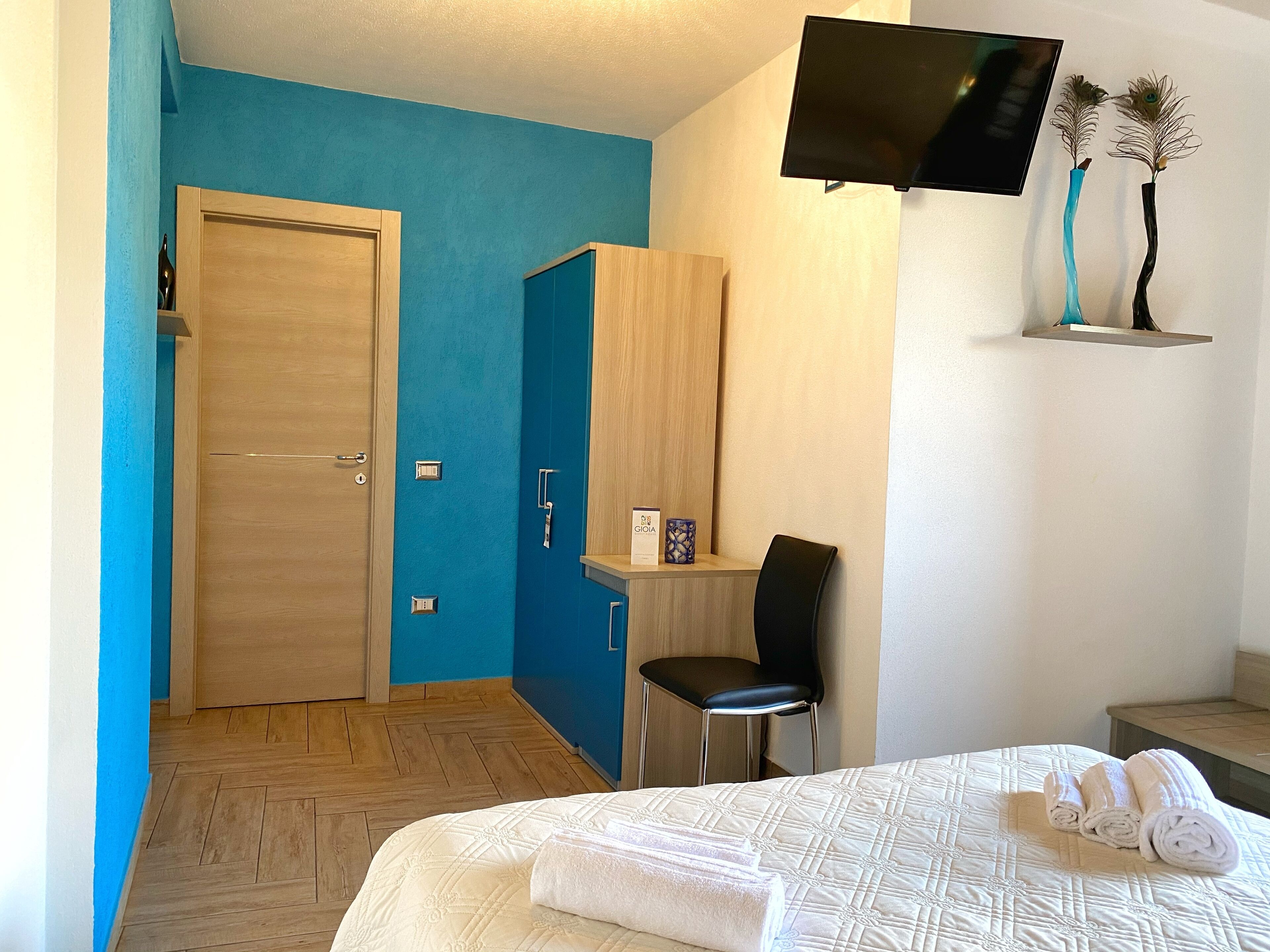 Una habitación de hotel con cama, escritorio, silla, televisor y estante con adornos.