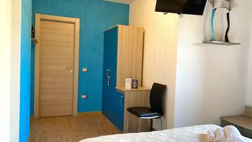 Una habitación de hotel con cama, escritorio, silla, televisor y estante con adornos.