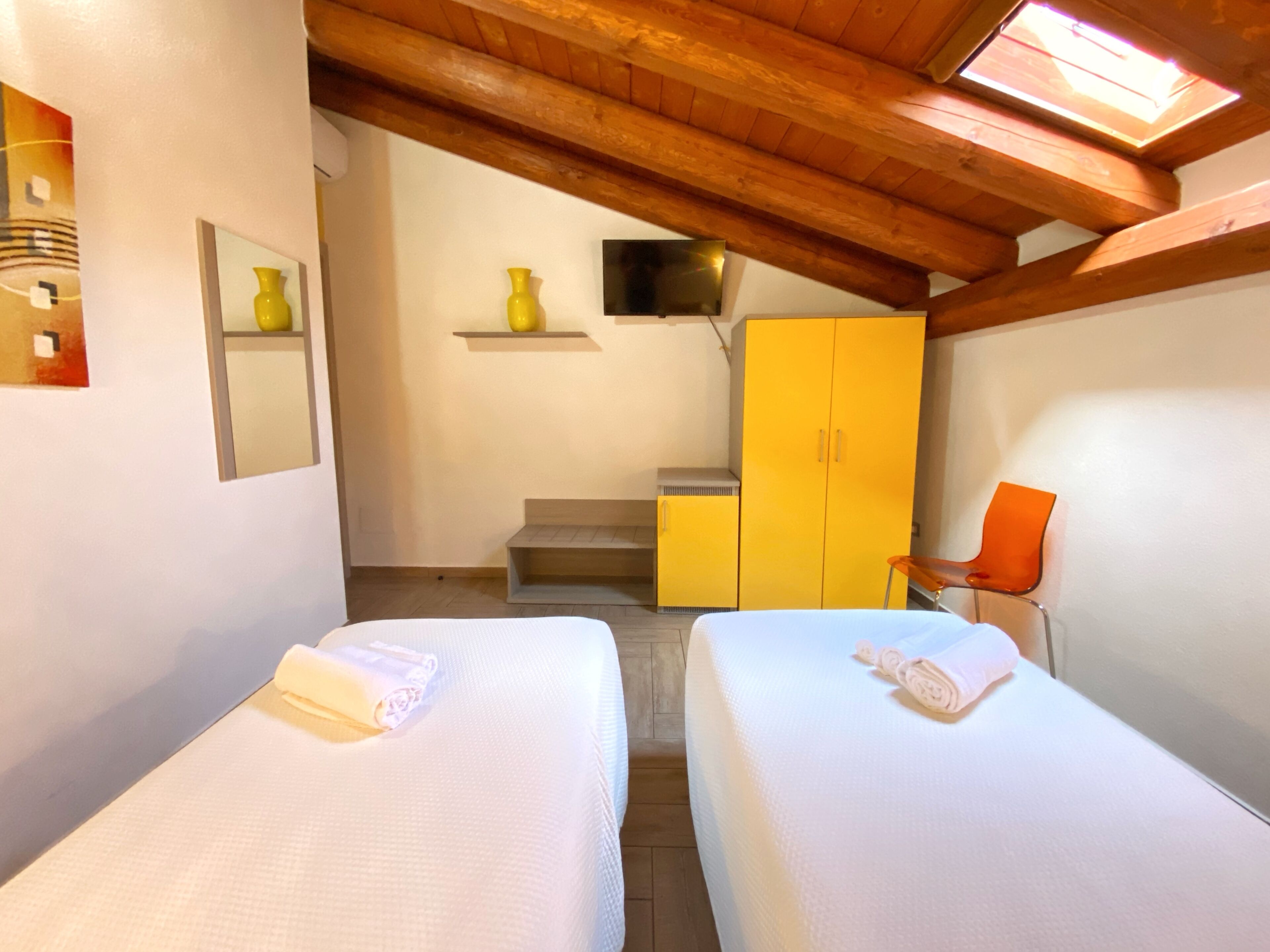 A bedroom with two beds, a wooden ceiling, a yellow wardrobe, and a small orange chair.