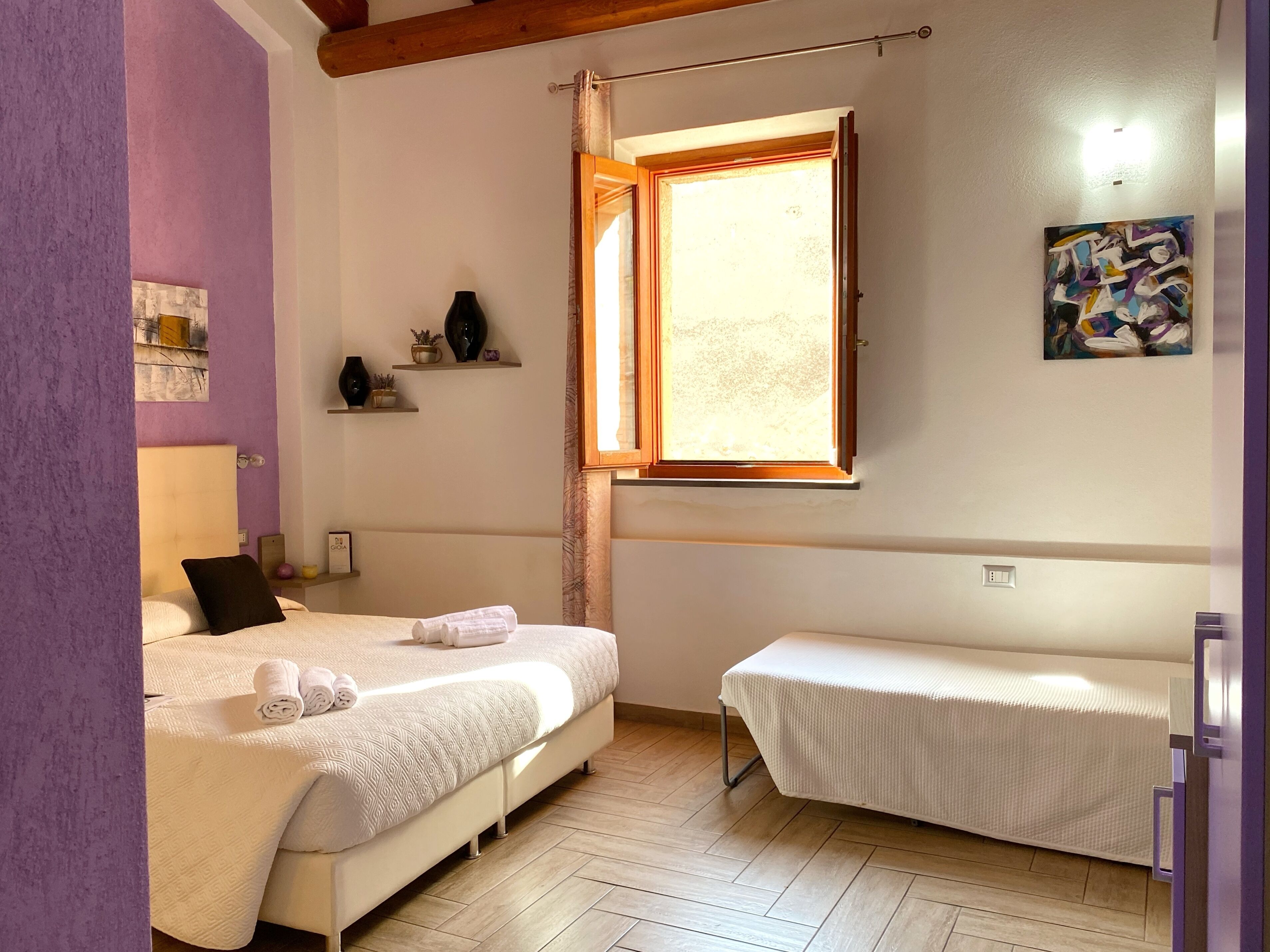 Une chambre avec un lit, un banc, une fenêtre et un tableau accroché au mur.