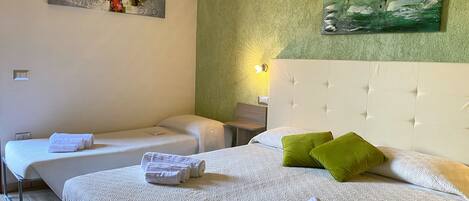 A hotel room with two single beds, a large bed with green pillows, and artwork on the walls.