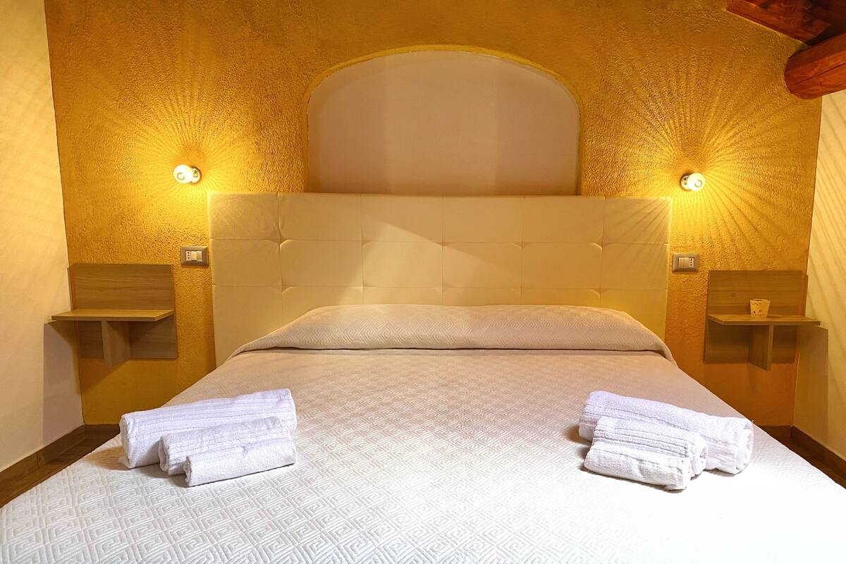 A neatly made bed with a white quilt, two towels on the bed, and two bedside lamps on either side.