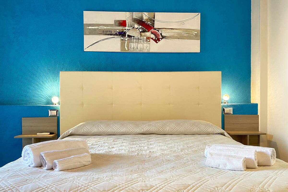 A neatly made bed with a quilted headboard, two bedside tables with lamps, and a painting on the wall.