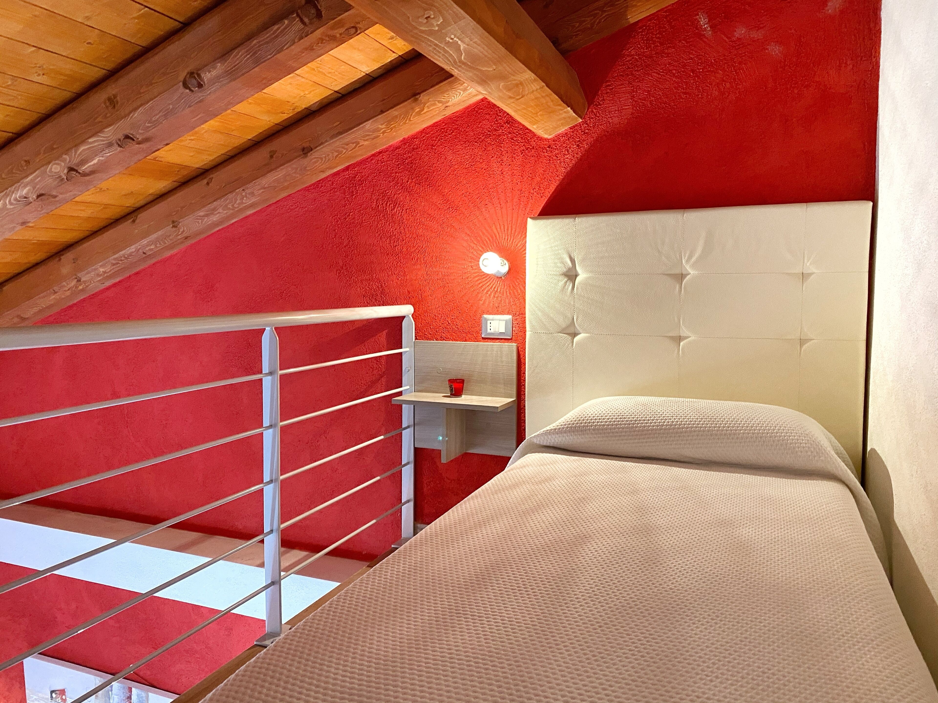 Un dormitorio con pared roja, cabecera blanca y techo de madera.
