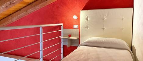 A bedroom with a red wall, a white headboard, and a wooden ceiling.