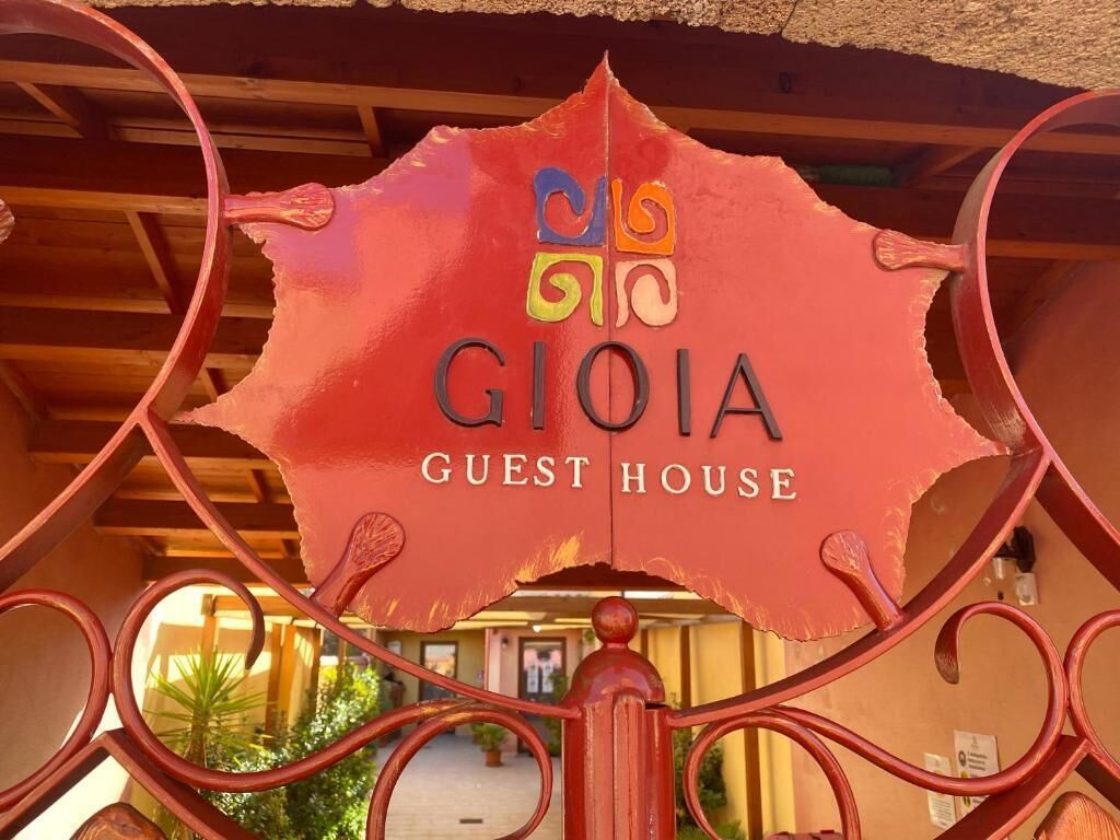 En röd skylt med texten ”GIOIA GUEST HOUSE” och en logotyp ovanför.