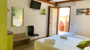 Habitación de hotel con una cama, una silla, un televisor, un espejo y una puerta que da a un espacio al aire libre.