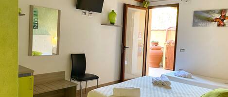 A hotel room with a bed, a chair, a TV, a mirror, and a door leading to an outdoor area.