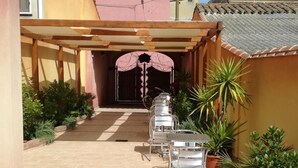 Un patio cubierto con mesas y sillas de metal, plantas en macetas y piso de baldosas.