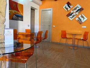 A modern guest room with a glass table, orange chairs, and artwork on the walls. - Gioia Guesthouse (Cabras)