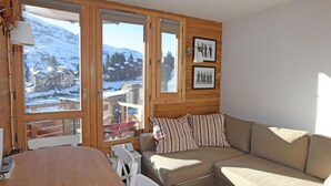 A cozy room with a wooden interior, a beige sofa, a dining table, and large windows offering a snowy mountain view. - Studio for 2 with balcony in the center of Avoriaz (Avoriaz)