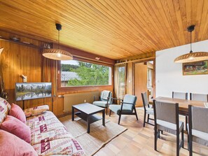 Ein gemütliches Blockhauss-Interieur mit Holzbalkendecke, einer Couch, einem Esstisch und Stühlen.