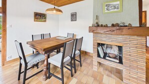 Een eetruimte met een houten tafel en stoelen, een metselwerk open haard en ingelijste foto's aan de muur.