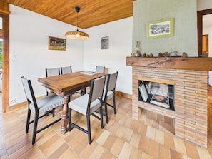 Ein Essbereich mit Holztisch und -stühlen, einem Kamin aus Backsteinen und gerahmten Bildern an den Wänden.