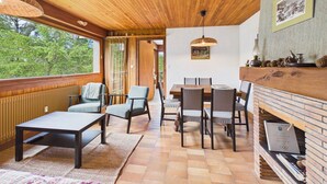 Een knus vertrek met een houten plafond, een eettafel met stoelen, een open haard en uitzicht op bomen.