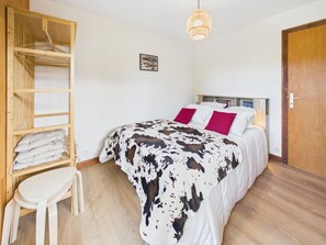 Ein Schlafzimmer mit einem Bett, einem Holzschrank, einem kleinen Hocker und einer Pendelleuchte.