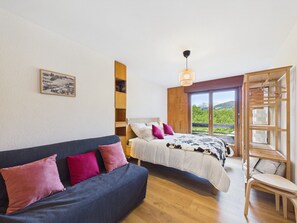 Una camera da letto con un letto, un divano, una mensola in legno, una lampada a sospensione e una finestra vista.