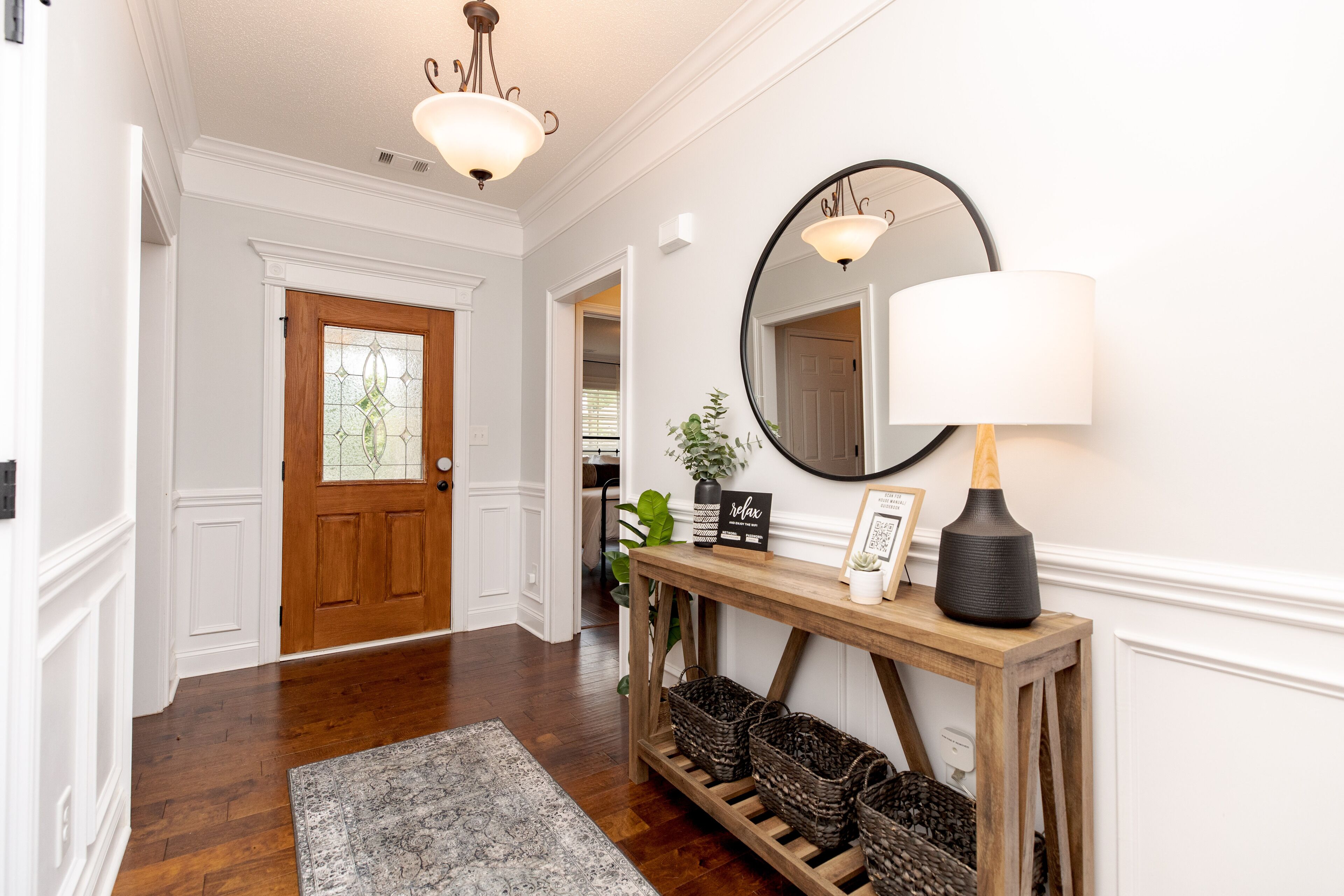 A hallway with a wooden door, a console table with baskets, a mirror, and a lamp.