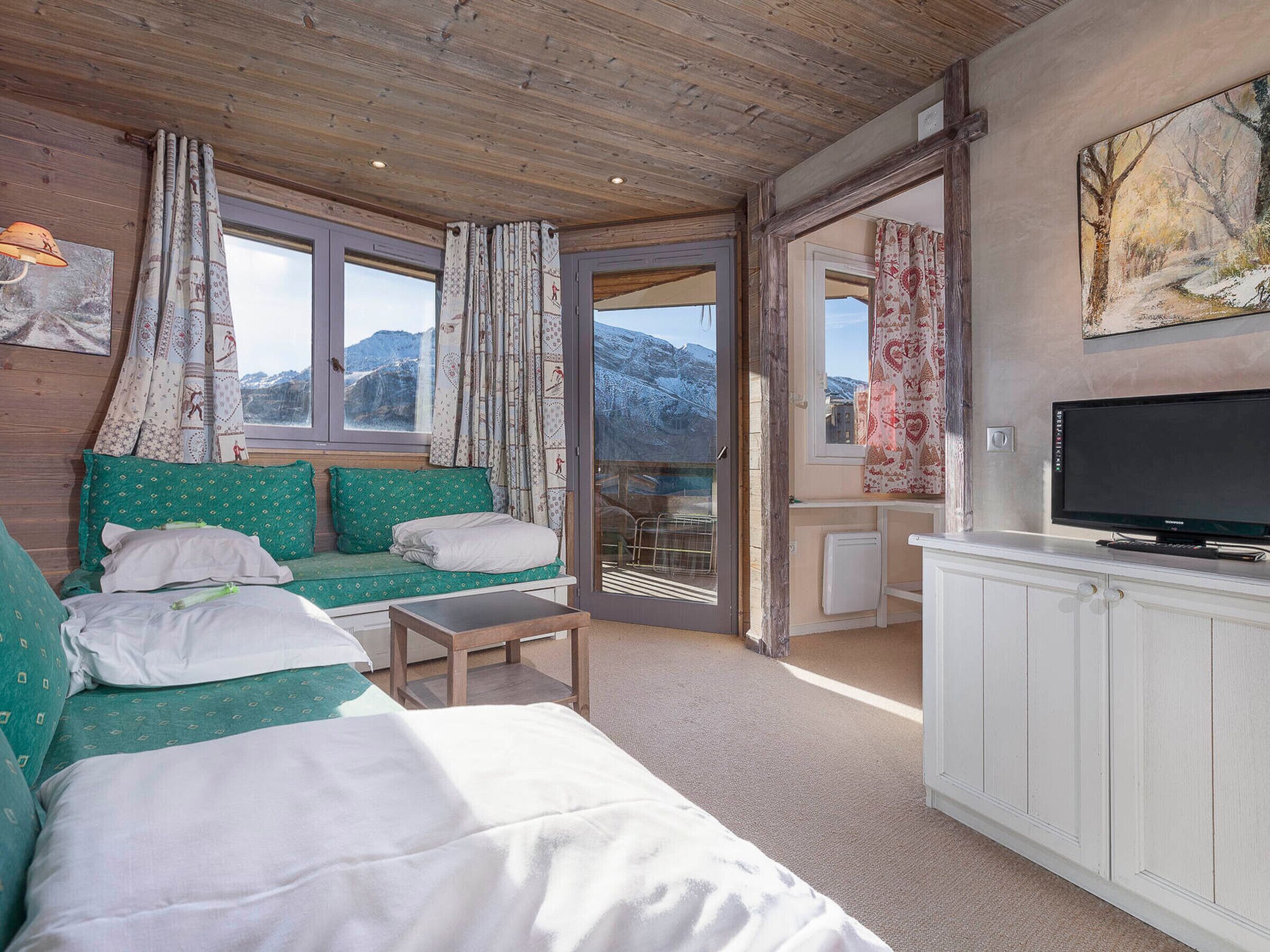 A cozy room with a sofa, a small table, a TV, and a view of mountains through a glass door.