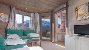 A cozy room with a sofa, a small table, a TV, and a view of mountains through a glass door. - Charming renovated apartment 2 rooms, balcony, WiFi (Avoriaz)