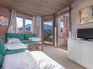 A cozy room with a sofa, a small table, a TV, and a view of mountains through a glass door. - Charming renovated apartment 2 rooms, balcony, WiFi (Avoriaz)