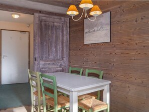 A dining area with a white table and green chairs, a wooden wall, and a painting.